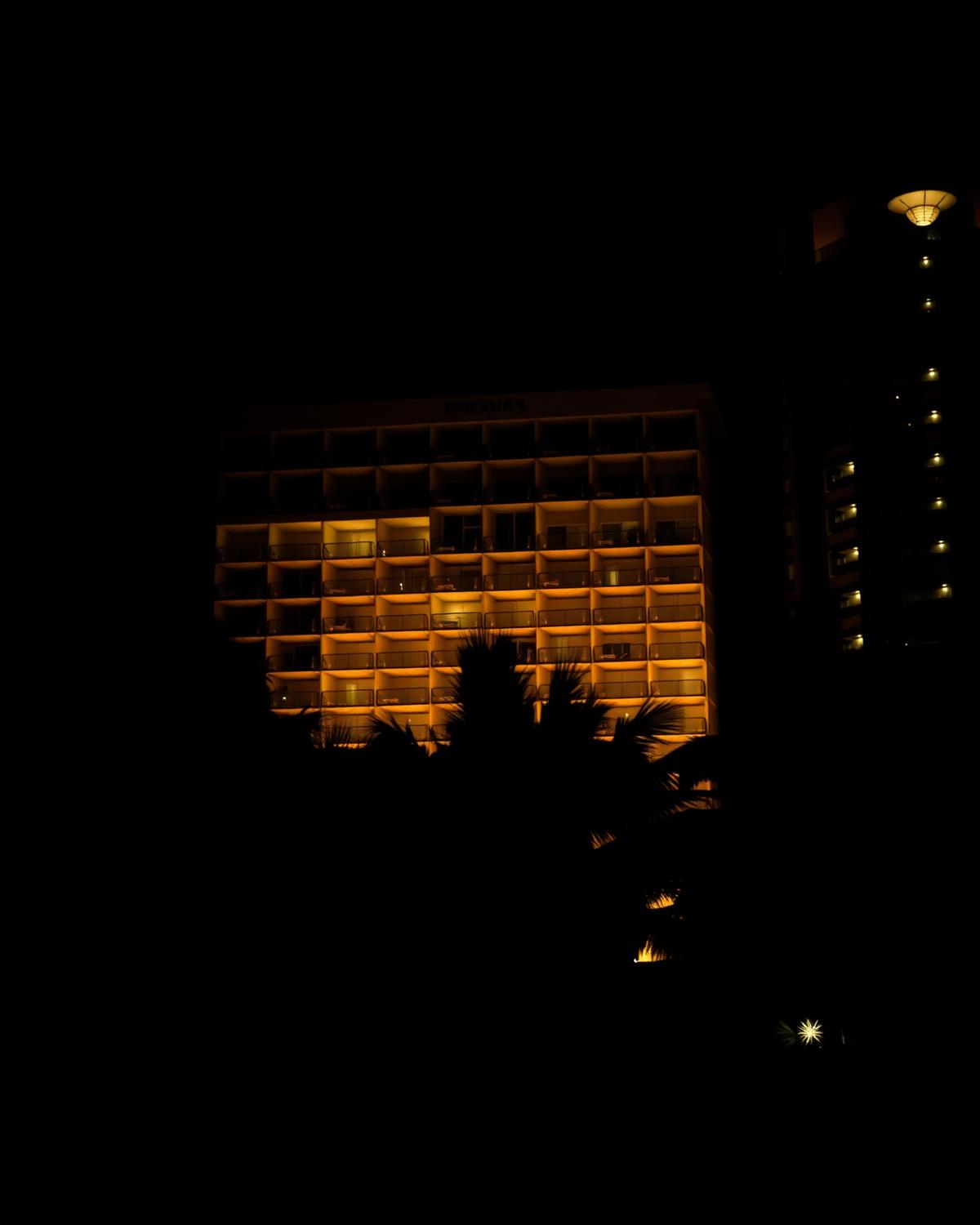 Waikiki resort balconies lit warmly at night behind palm silhouettes